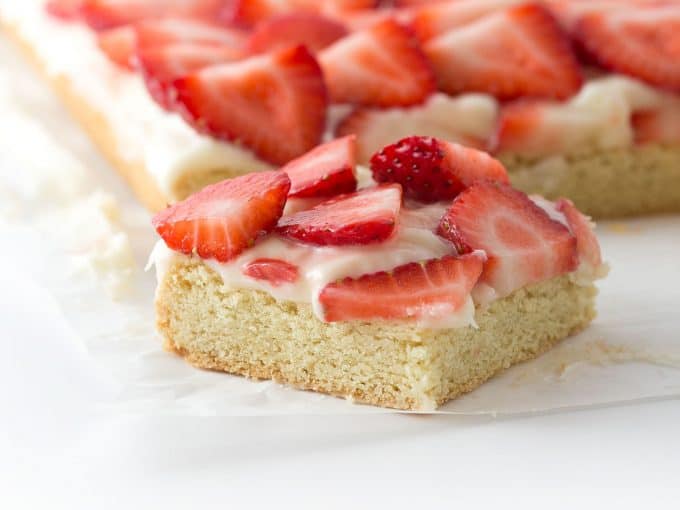 cut square of sugar cookie bars topped with frosting and sliced strawberries