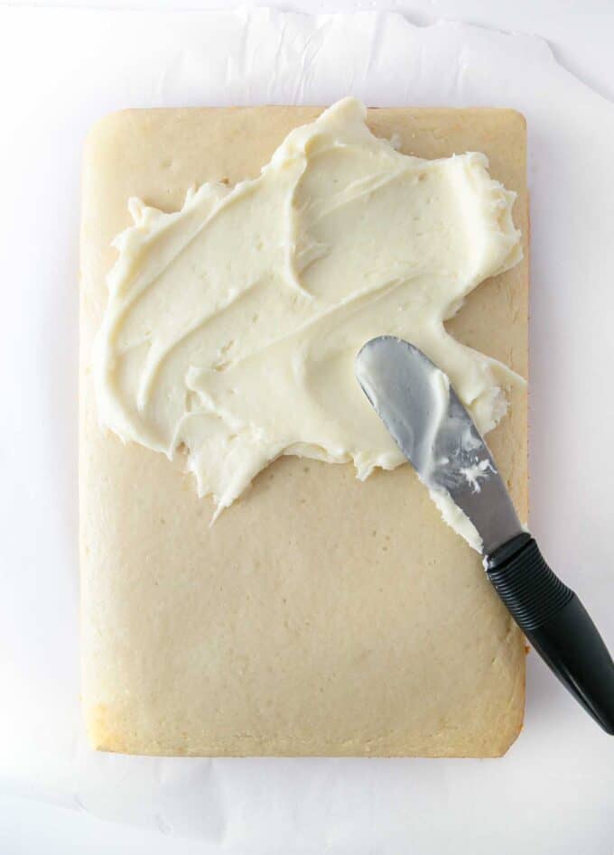 overhead photo of white 9x13 sheet cake with spatula spreading on white frosting