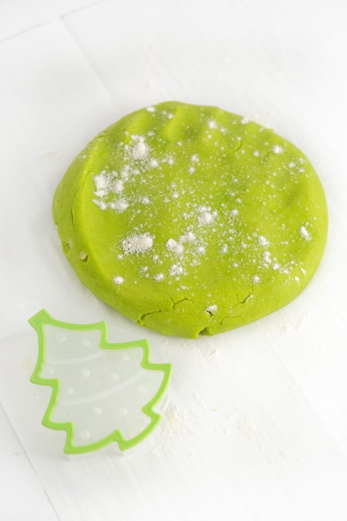 ball of green sugar cookie dough with christmas tree cookie cutter
