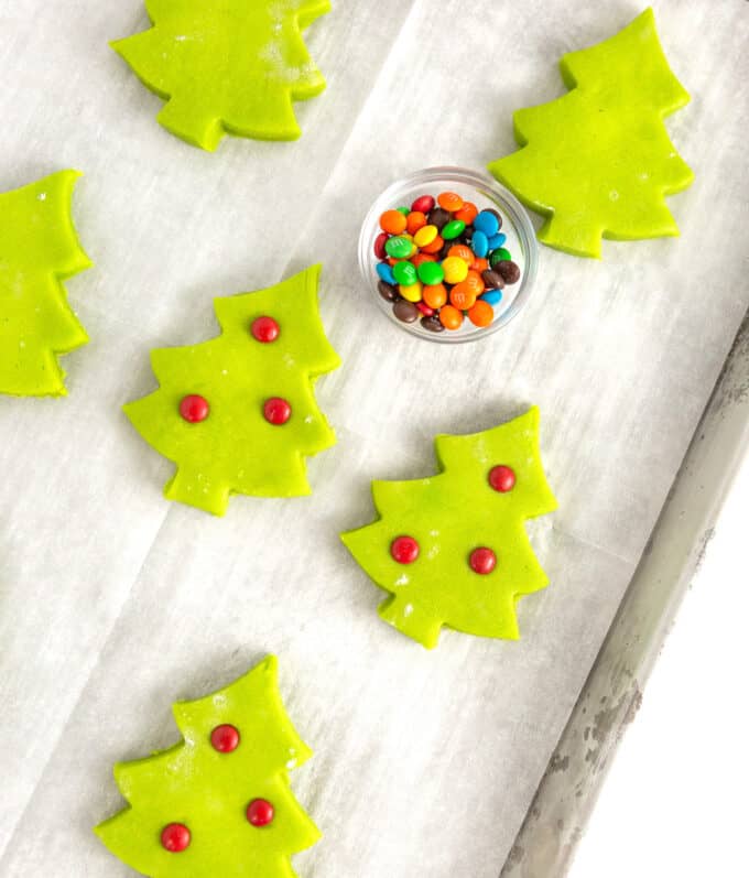 baking pan of green christmas tree sugar cookie with red M&M ornaments pressed into top