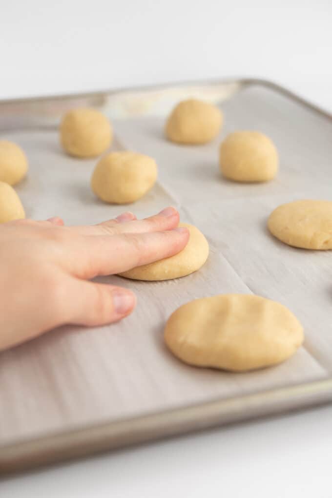 hand pressing sugar cookie dough ball to flatten