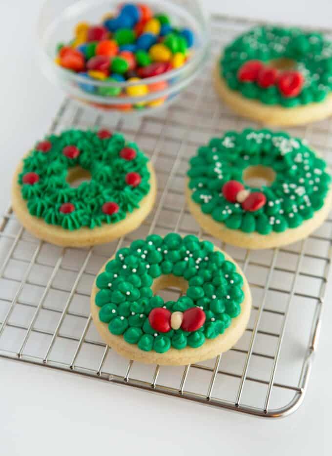 green buttercream wreath sugar cookies on metal cooling rack with red m&m candy to make a bow