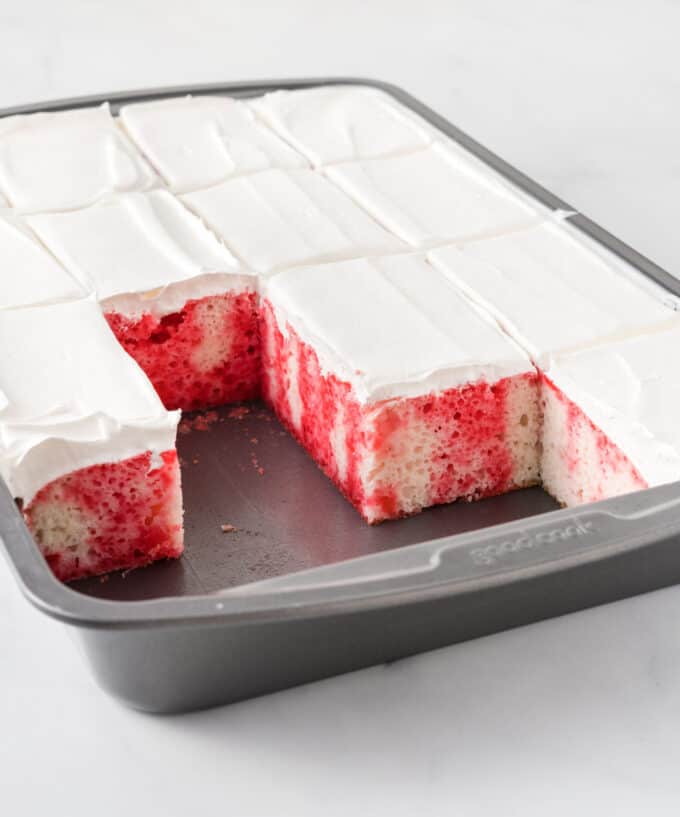 Sliced strawberry poke cake in metal cake pan with several pieces removed 