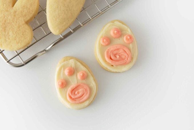 Easter egg shaped sugar cookie decorated with white frosting and three pink dots to look like bunny paw