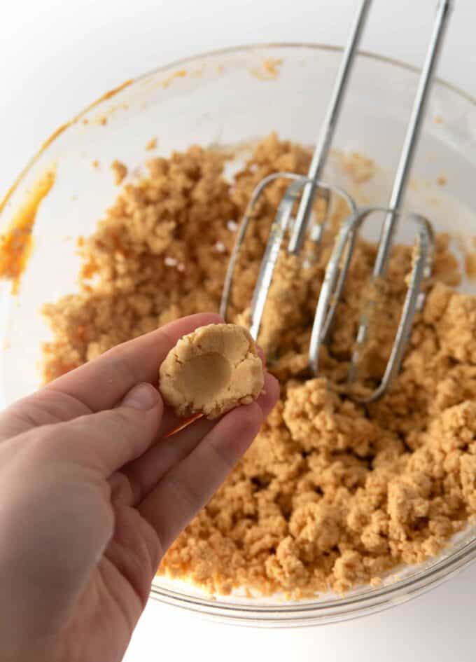 bowl of homemade peanut butter egg dough with thumb pressing in dough to show playdoh texture