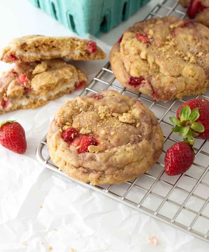 Strawberry Cheesecake cookies are stacked on a metal cooling rack, surrounded by strawberries.