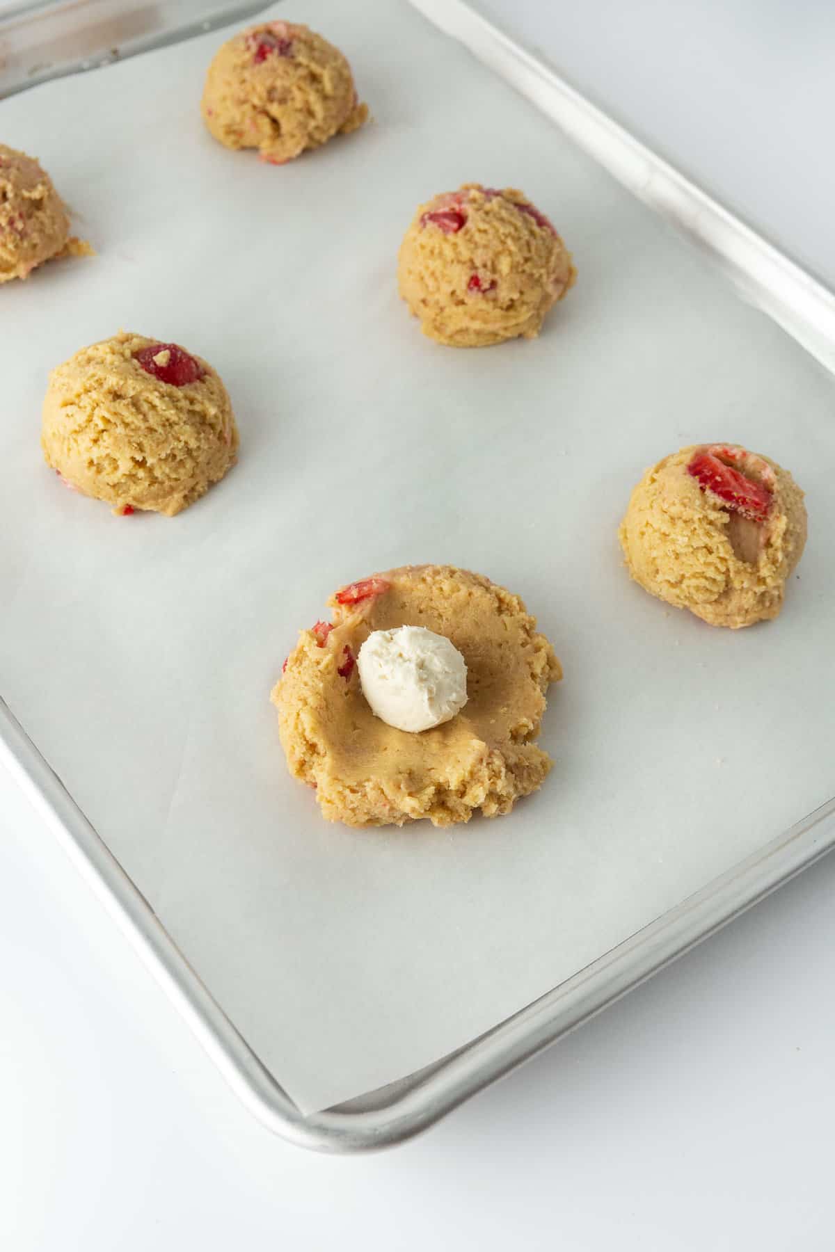 Strawberry Cheesecake cookies are stacked on a metal cooling rack, surrounded by strawberries. 