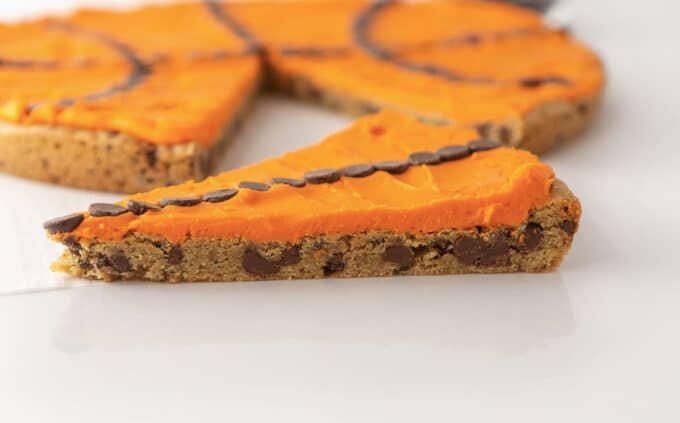 Slice of chocolate chip cookie cake decorated with orange frosting and chocolate chips