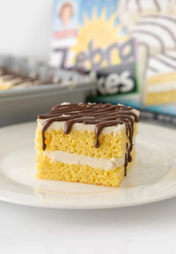 Square of homemade zebra cake on plate with box of Little Debbie zebra cakes in background