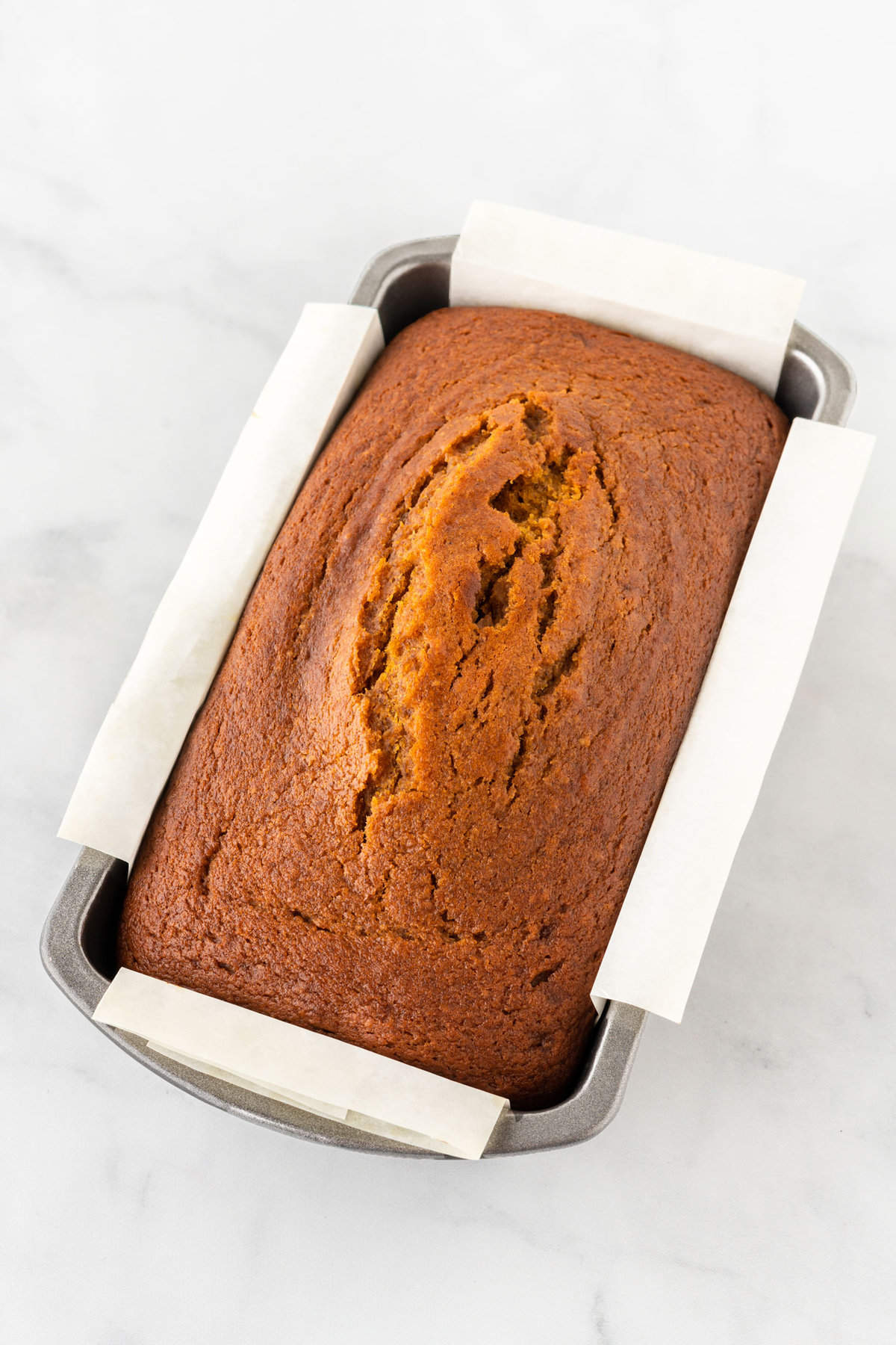 baked pumpkin bread in metal loaf pan with parchment sling