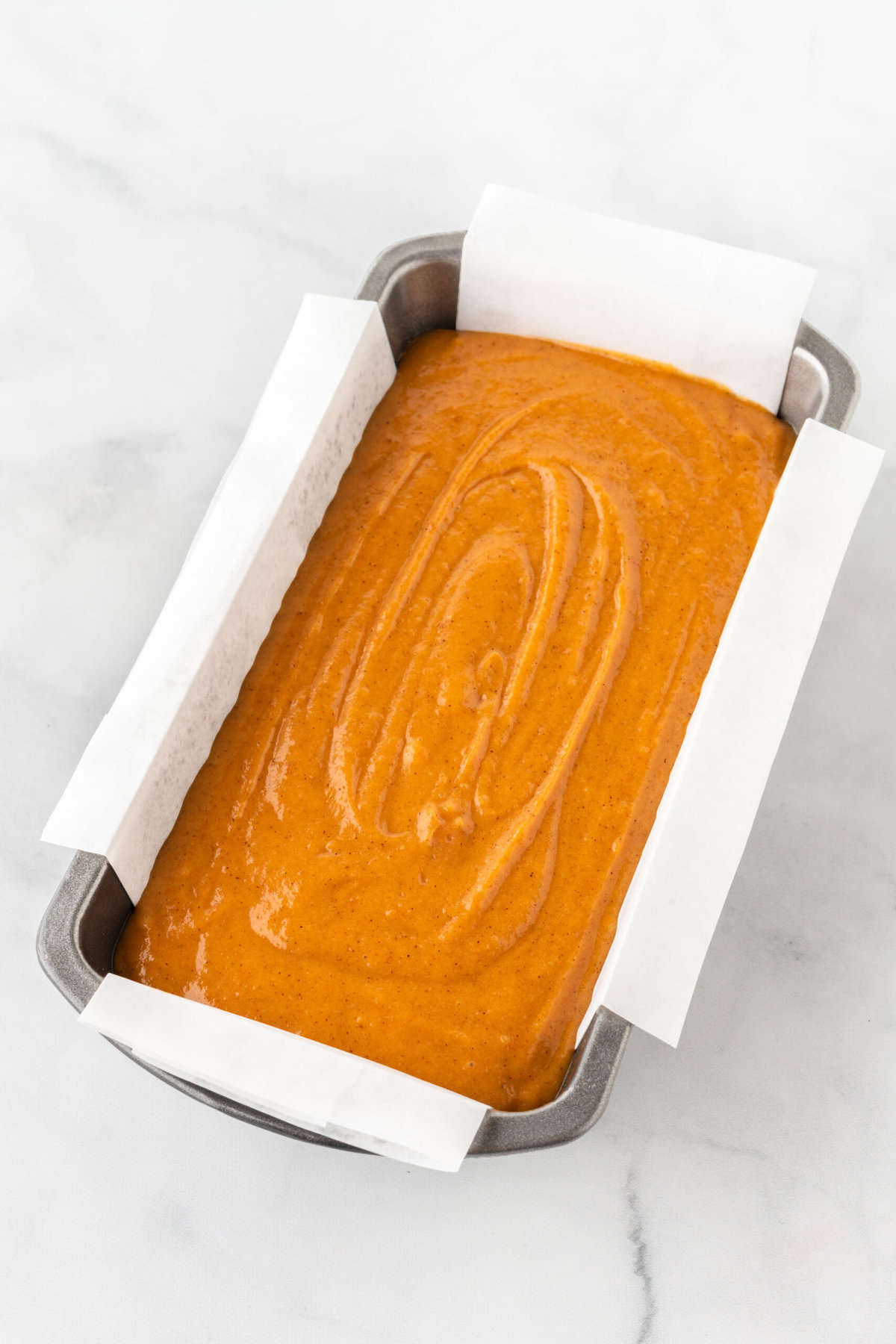 pumpkin bread batter in metal loaf pan with parchment sling