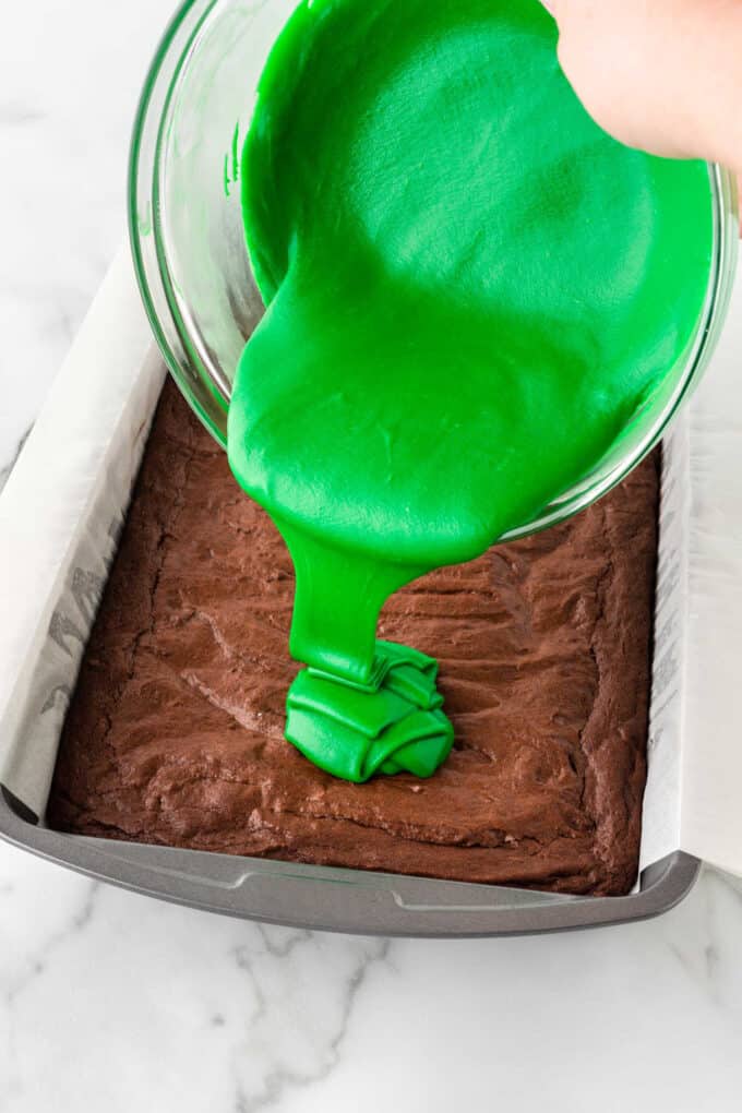 pouring green white chocolate on pan of brownies
