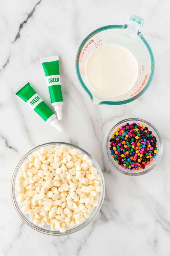 bowl of white chocolate chips, green food coloring, heavy cream, and rainbow chip sprinkles for Little Debbie brownie trees