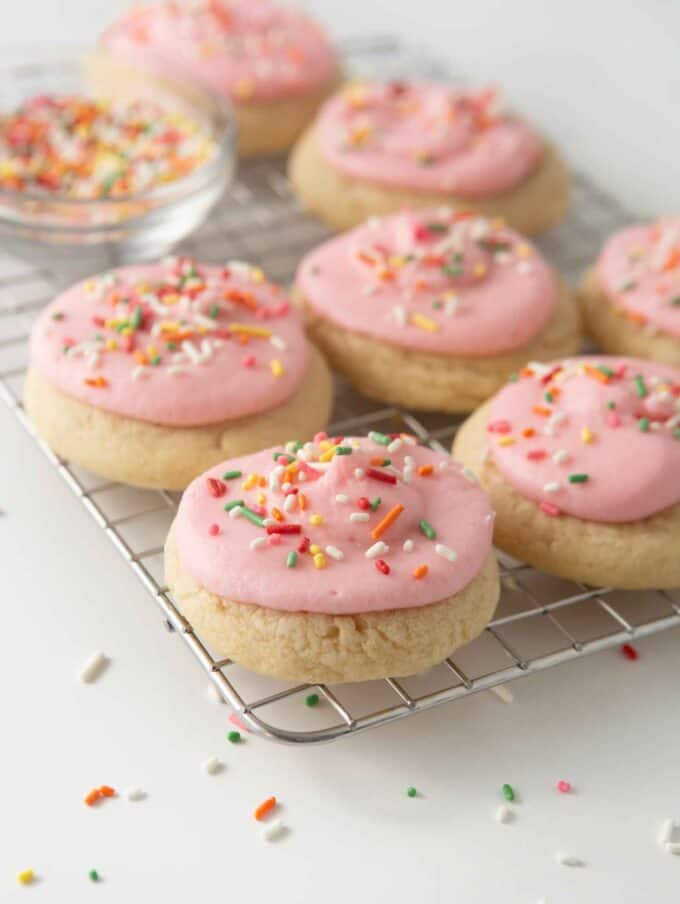 soft frosted sugar cookies on cooling rack with pink frosting and rainbow sprinkles