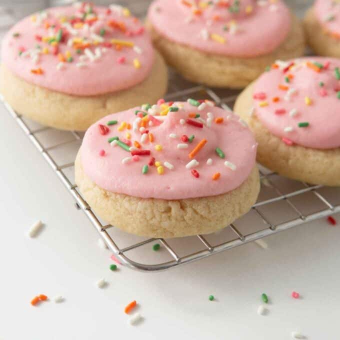 soft frosted sugar cookies on cooling rack with pink frosting and rainbow sprinkles