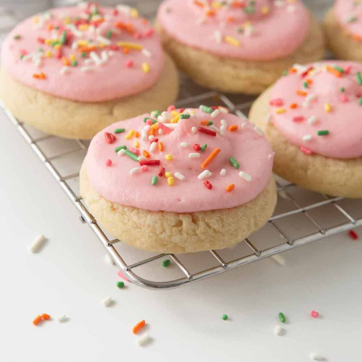 soft frosted sugar cookies on cooling rack with pink frosting and rainbow sprinkles