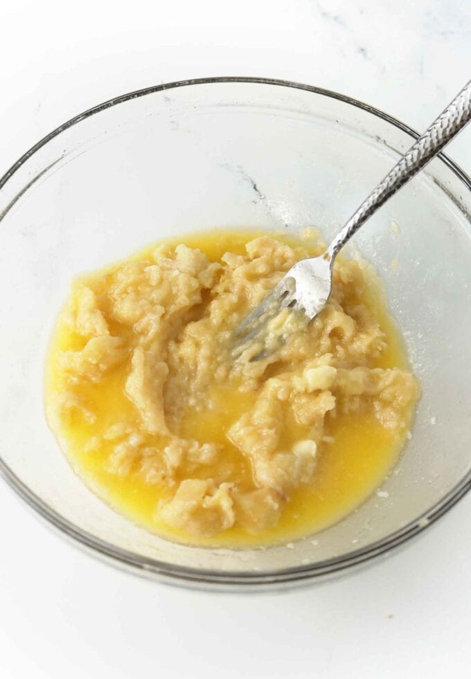 glass bowl of mashed bananas with melted butter and fork