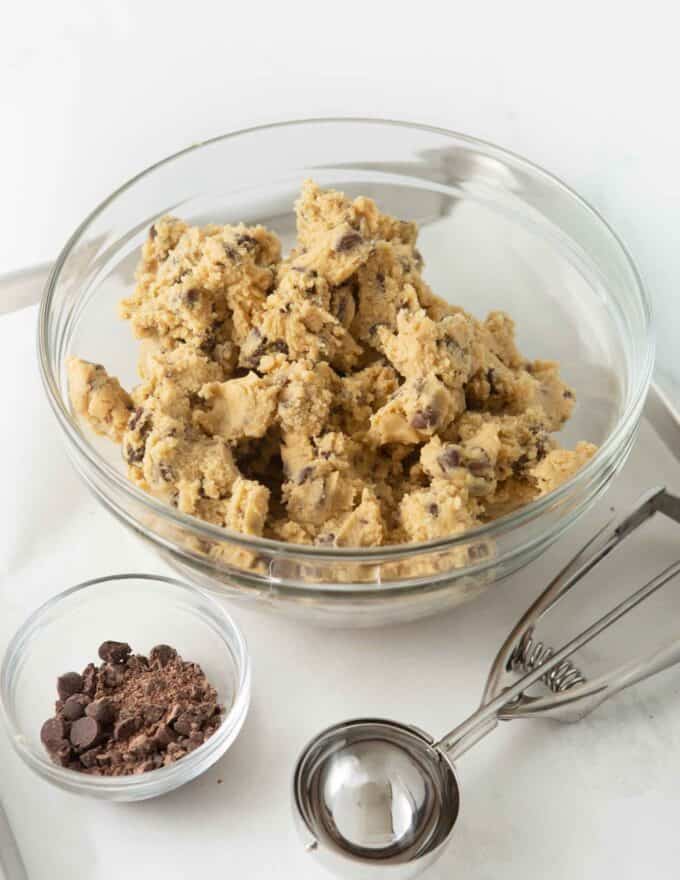 bowl of chocolate chip cookie dough with cookie scoop and bowl of chopped chocolate for rolling