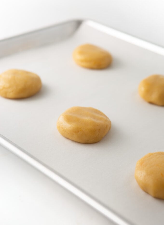 orange sugar cookie dough balls slightly flattened on cookie sheet