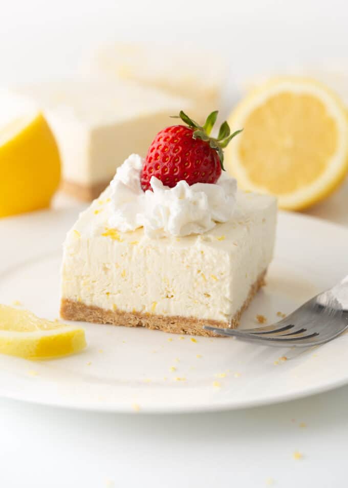 square of no bake lemon cheesecake on plate with whipped cream and strawberry on top