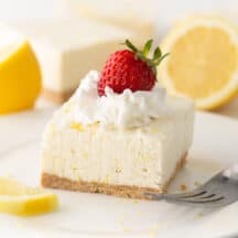 square of no bake lemon cheesecake on plate with whipped cream and strawberry on top