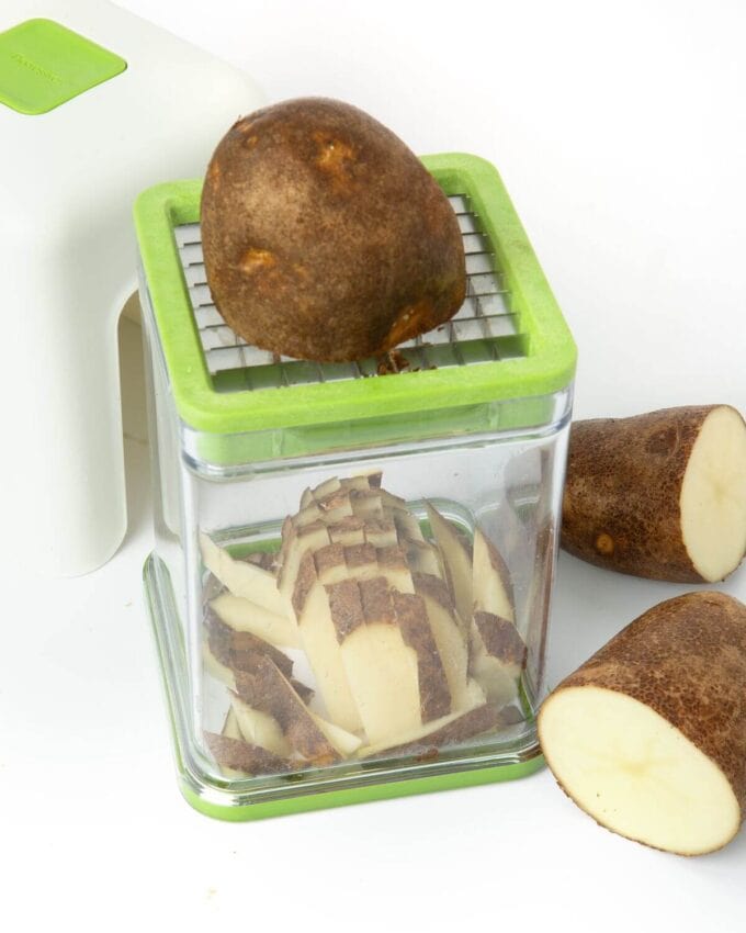 raw potato being cut with french fry cutter
