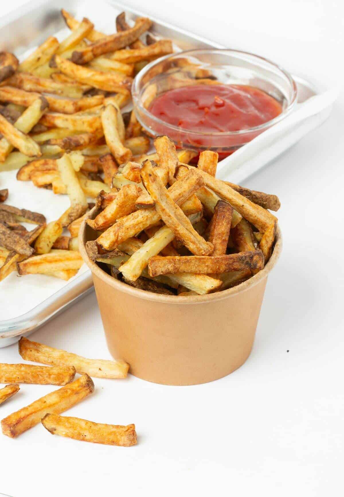 air fryer french fries in small paper bowl with baking tray and bowl of ketchup