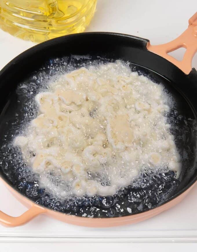 funnel cake batter being fried in hot oil in pink skillet