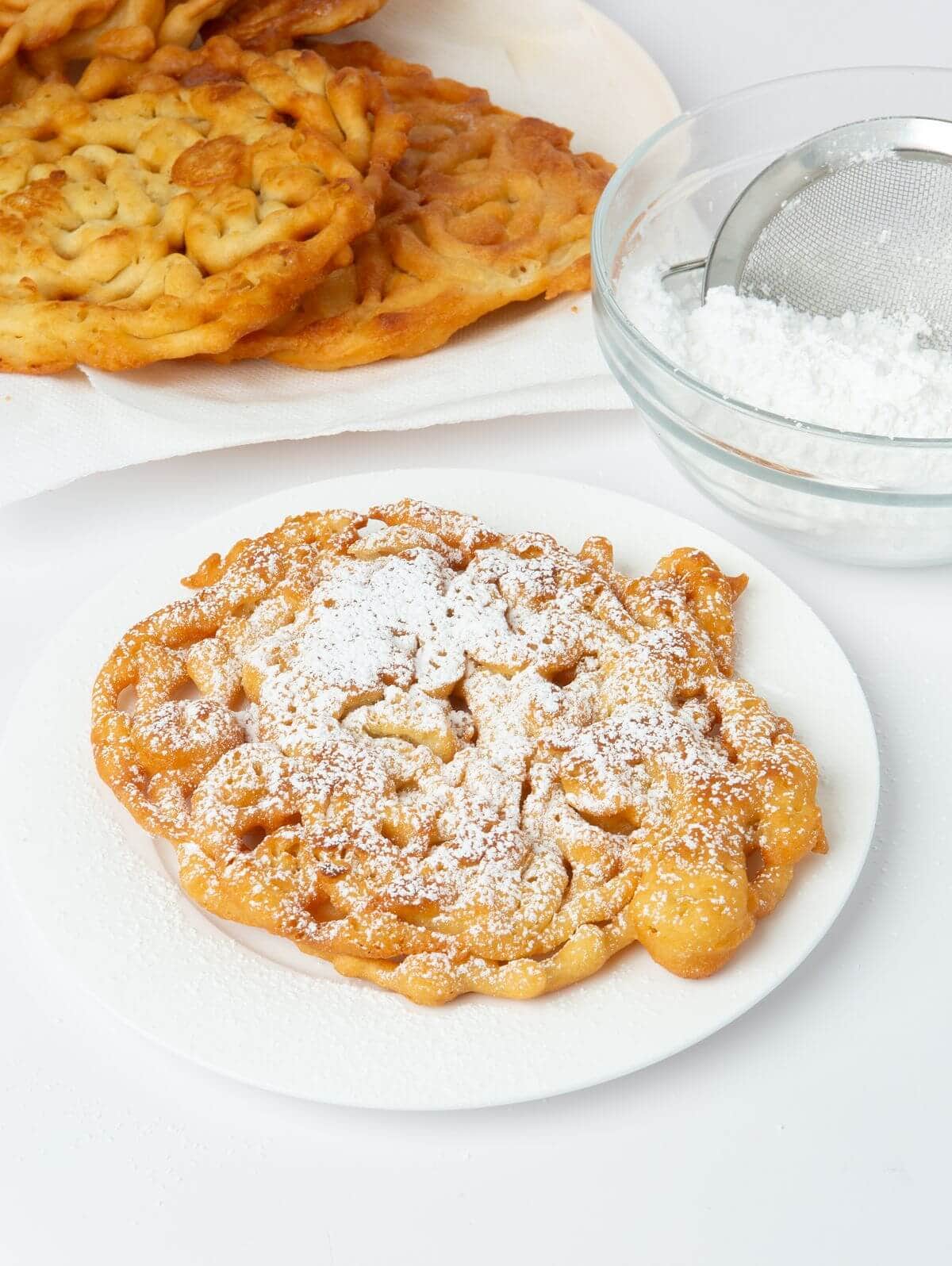 funnel cake on white plate with powdered sugar