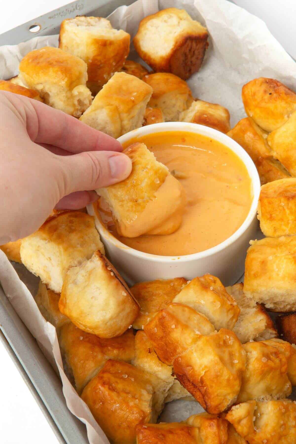 hand dipping pretzel bite monkey bread in cheese sauce