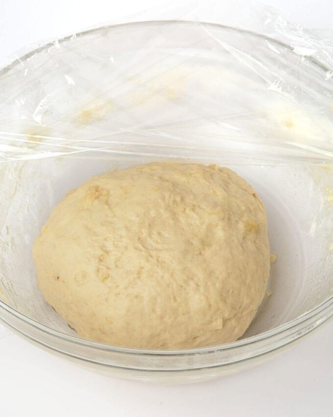 proofed pretzel bite dough in glass bowl with plastic wrap