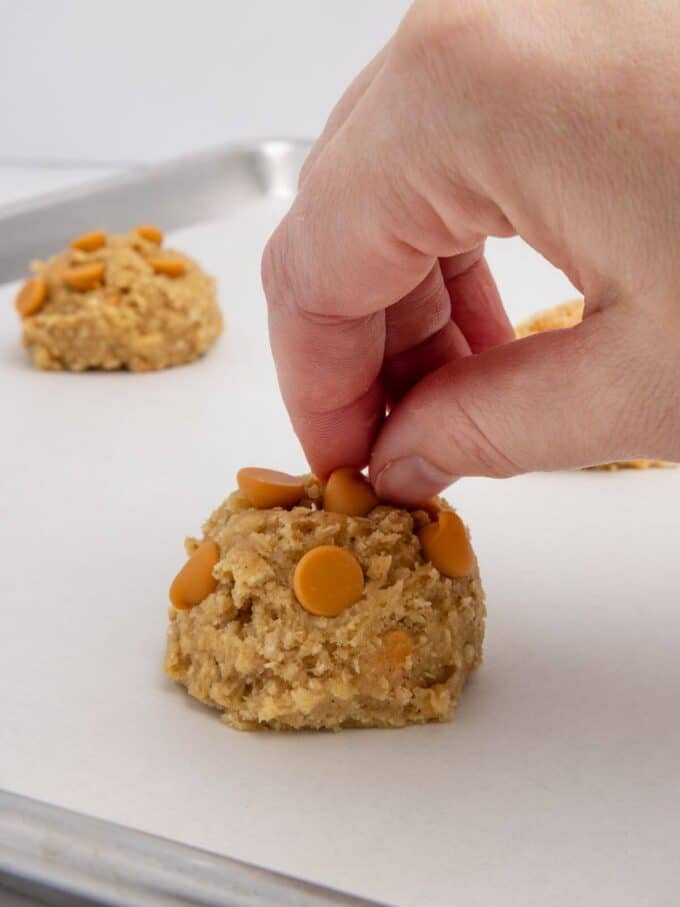 placing butterscotch chips on scoop of oatmeal scotchie cookie dough on parchment lined baking sheet