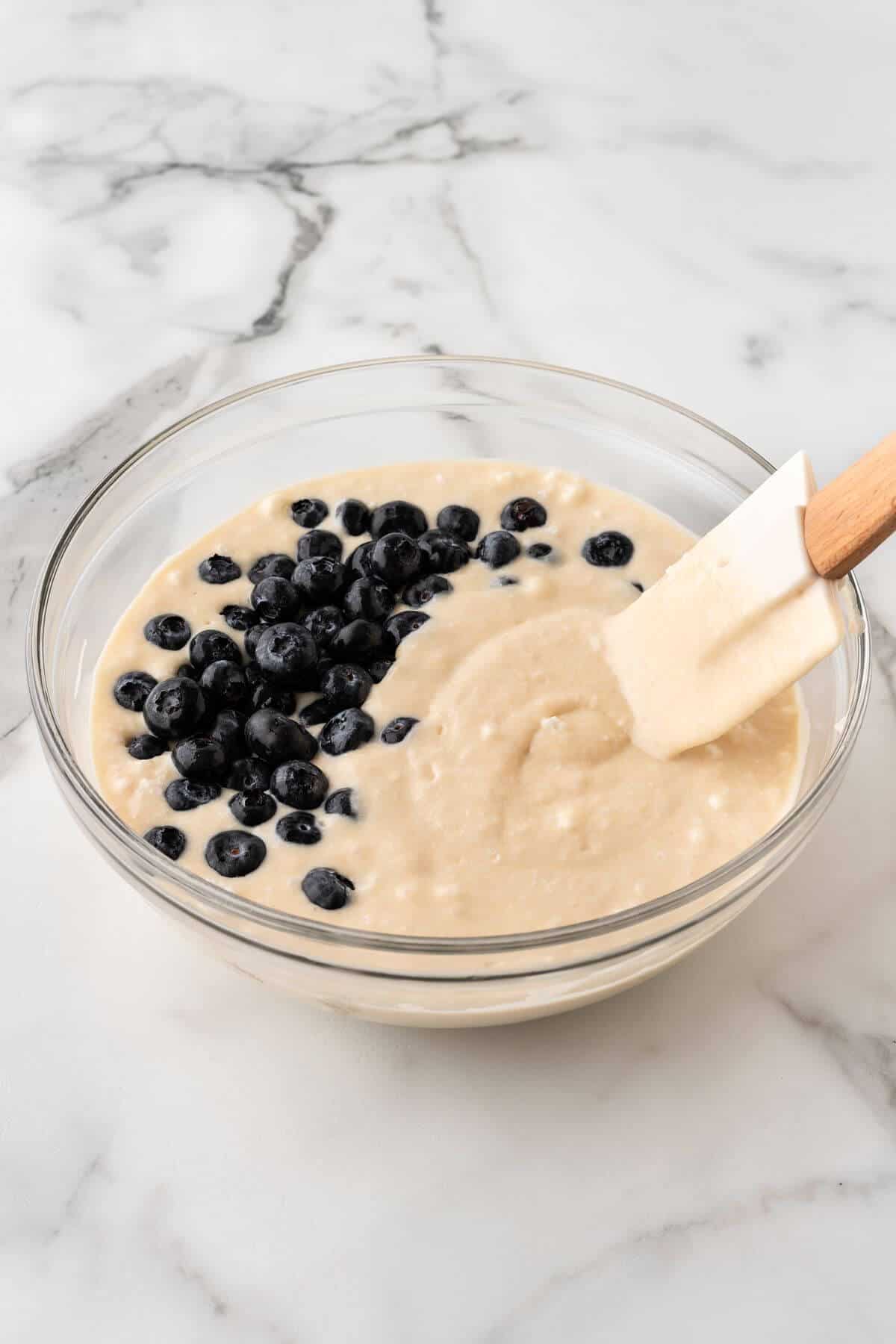 Adding blueberries to waffle batter in mixing bowl.
