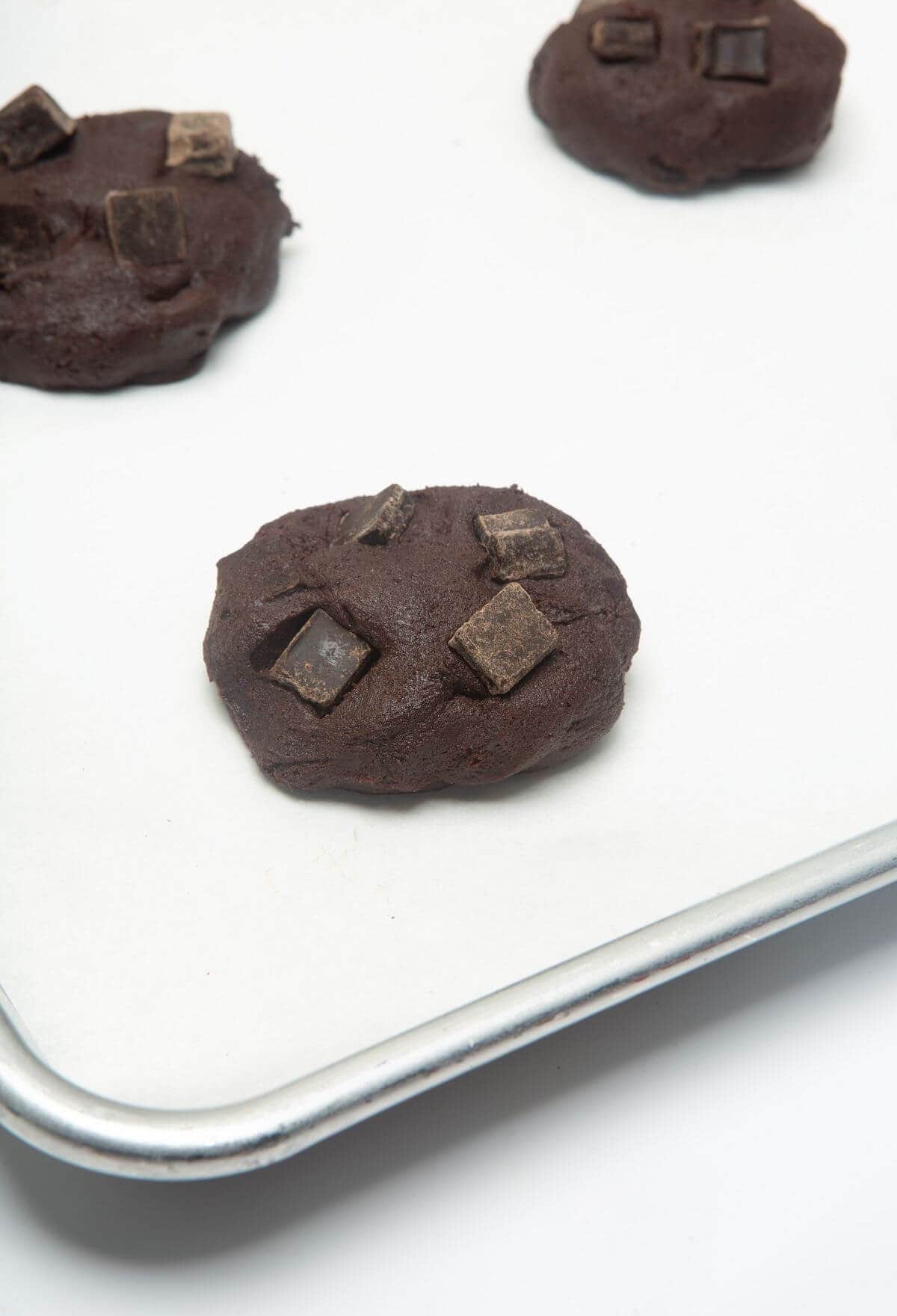 Raw dark chocolate cookies on parchment-lined baking sheet.