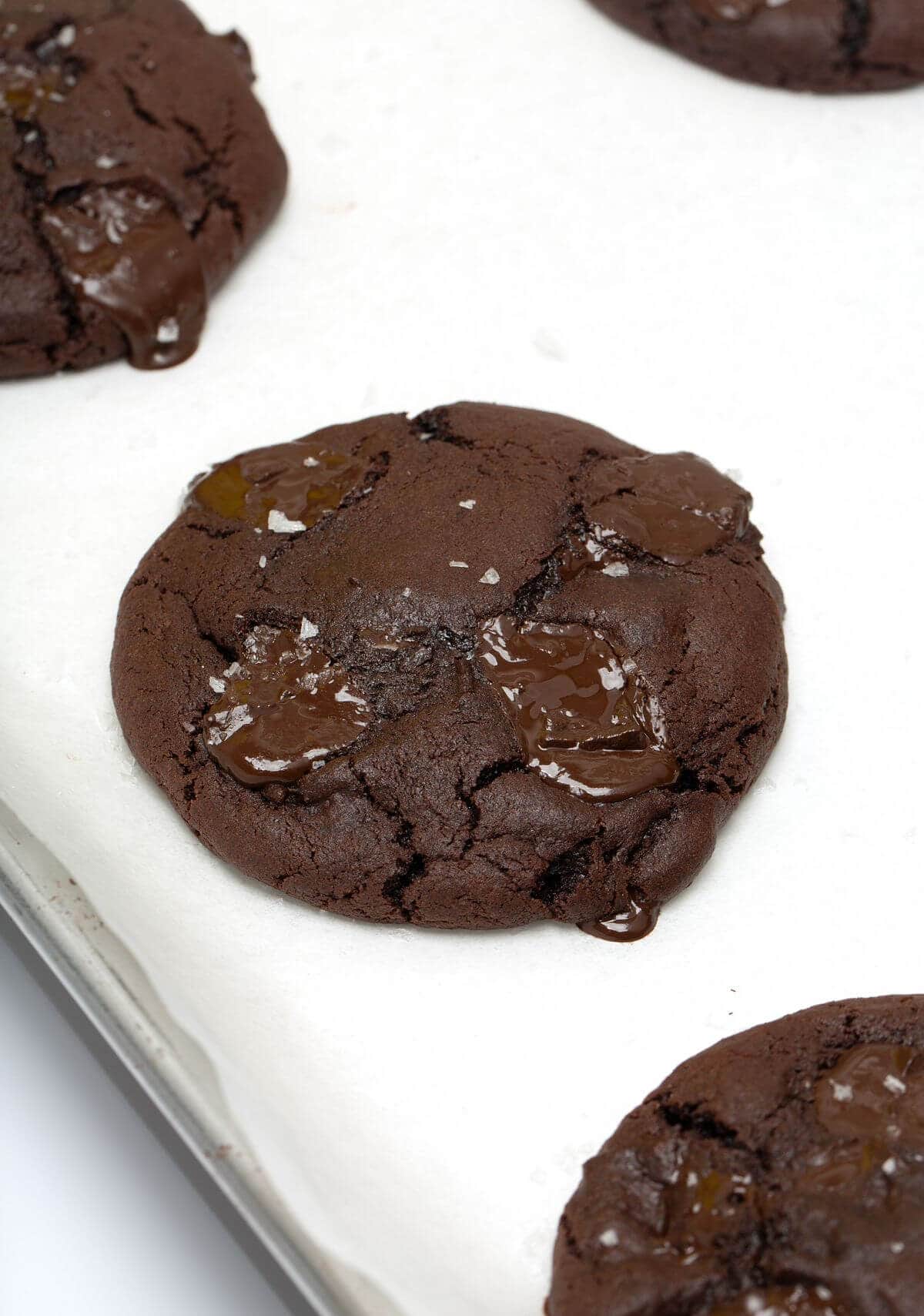 Baked dark chocolate cookie on parchment-lined baking sheet.