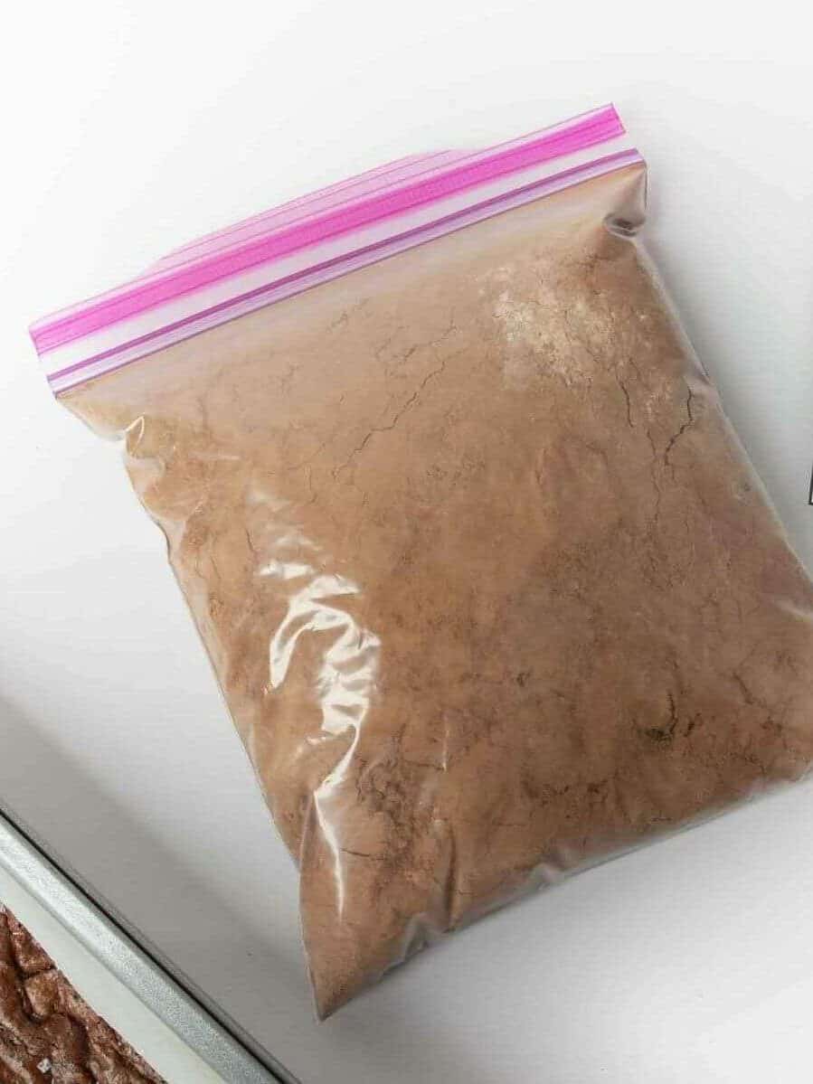 Sealed bag of homemade brownie mix with a printed label showing baking instructions, next to a pan of baked brownies