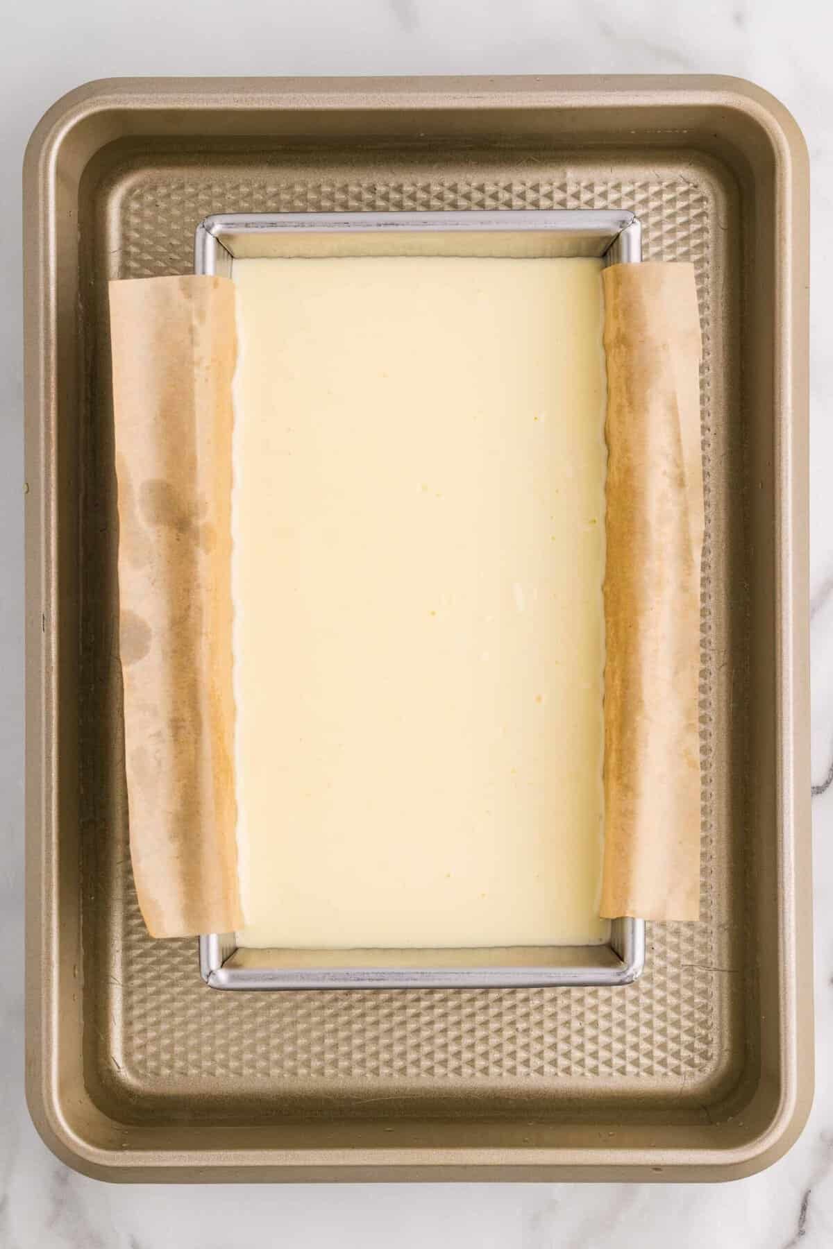 Overhead view of a parchment-lined loaf pan filled with cheesecake batter sitting inside a larger baking pan for a water bath, ready to go into the oven