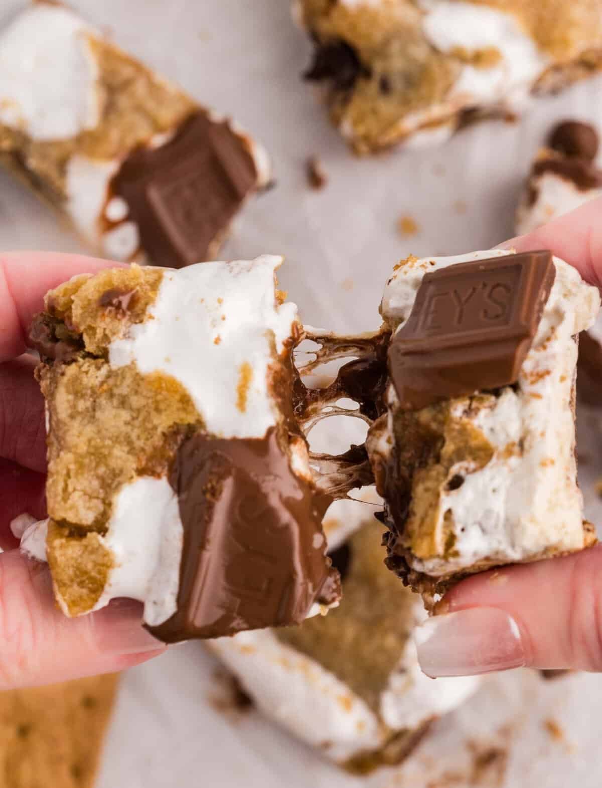 Hand holding a Stuffed S'mores Bar showing the gooey marshmallow fluff and graham cracker layer between cookie dough