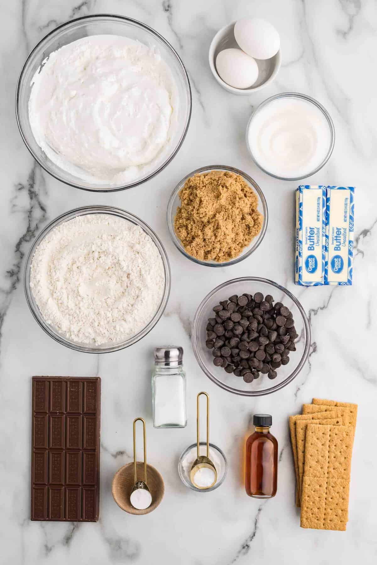 Ingredients for Stuffed S'mores Bars flat lay including graham crackers, marshmallow fluff, Hershey's bar, butter, sugar, eggs, vanilla, flour, and chocolate chips