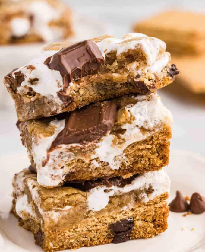 Stuffed S'mores Bars stacked vertically showing the hidden graham cracker and marshmallow fluff layer between two cookie dough layers, topped with Hershey's chocolate