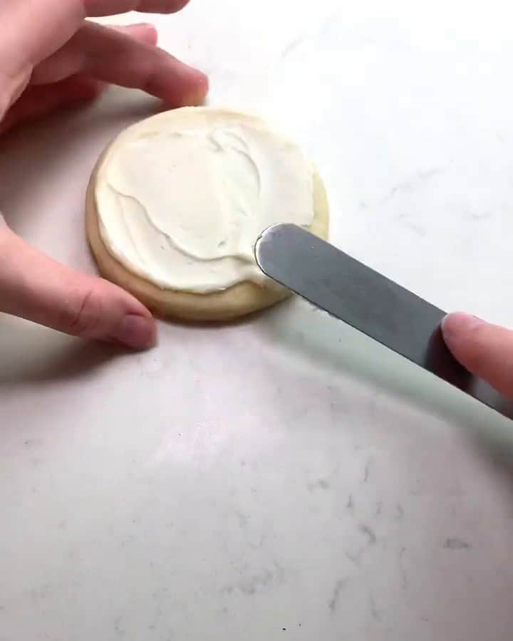 Spreading white buttercream on a round sugar cookie