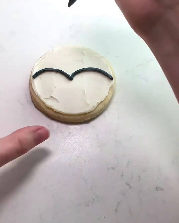 Piping a black heart-shaped outline on the white penguin cookie