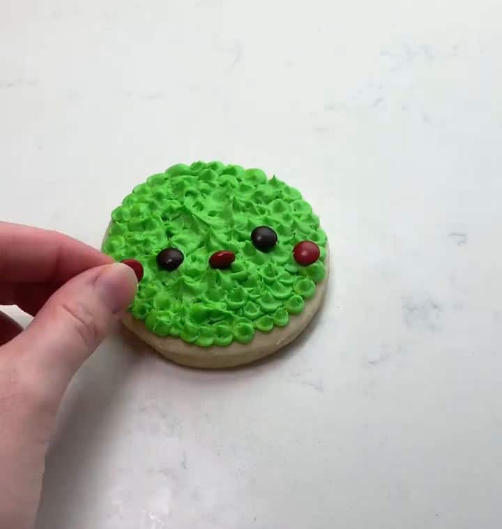 Pressing candy eyes and red cheeks onto the green Grinch cookie