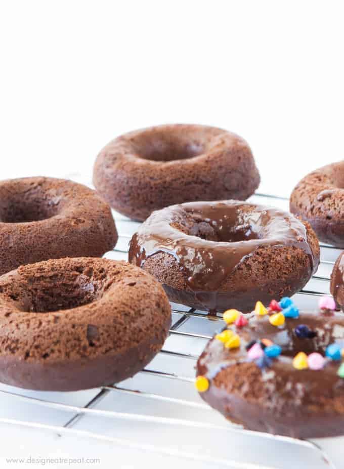 Cosmic Triple Chocolate Cake Donuts on wire rack with rainbow sprinkles and chocolate ganache glaze