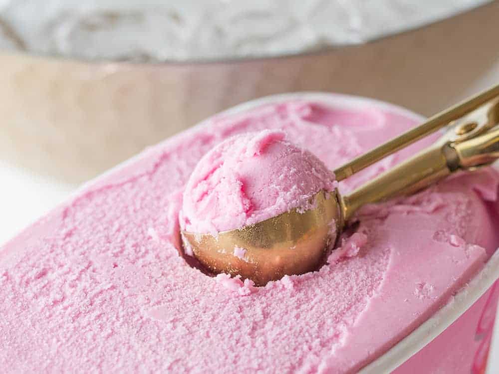 Scooping raspberry sherbet in carton with gold ice cream scoop.