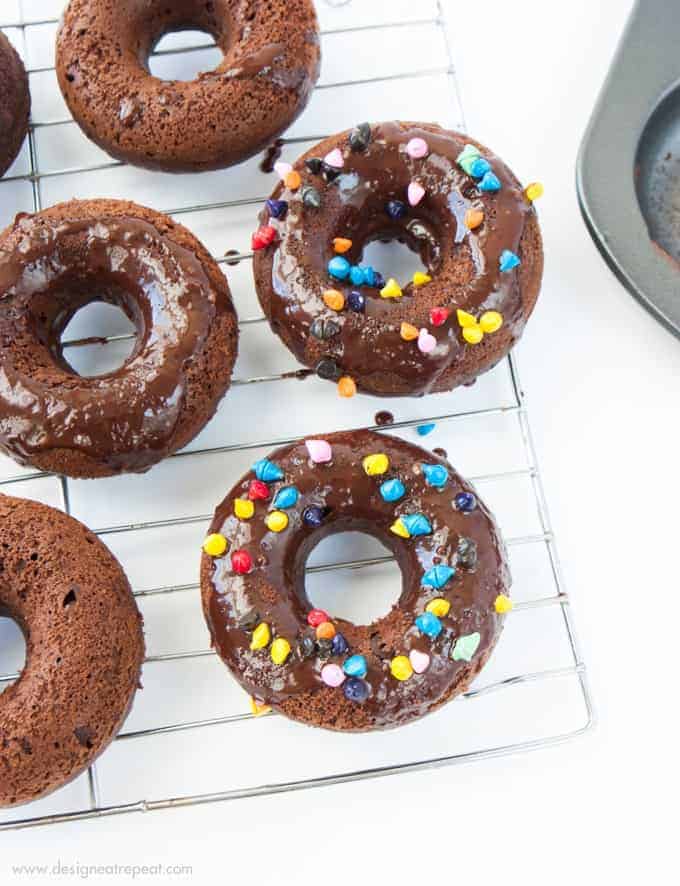 Cosmic Triple Chocolate Cake Donuts on wire rack with rainbow sprinkles