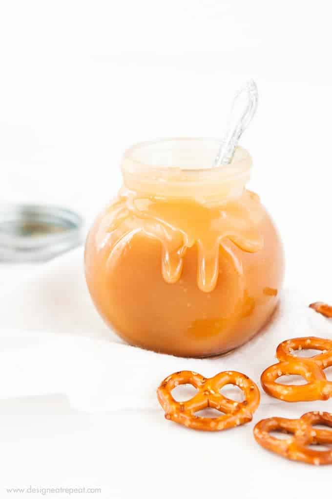 Jar of Microwave Salted Caramel Sauce with spoon and pretzels.