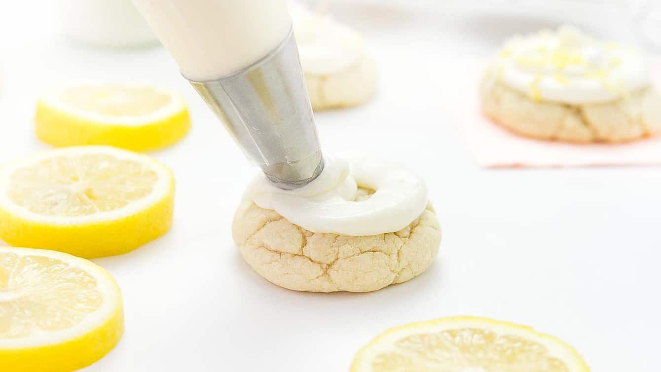 Piping bag and tip piping cream cheese frosting onto thick lemon sugar cookie.