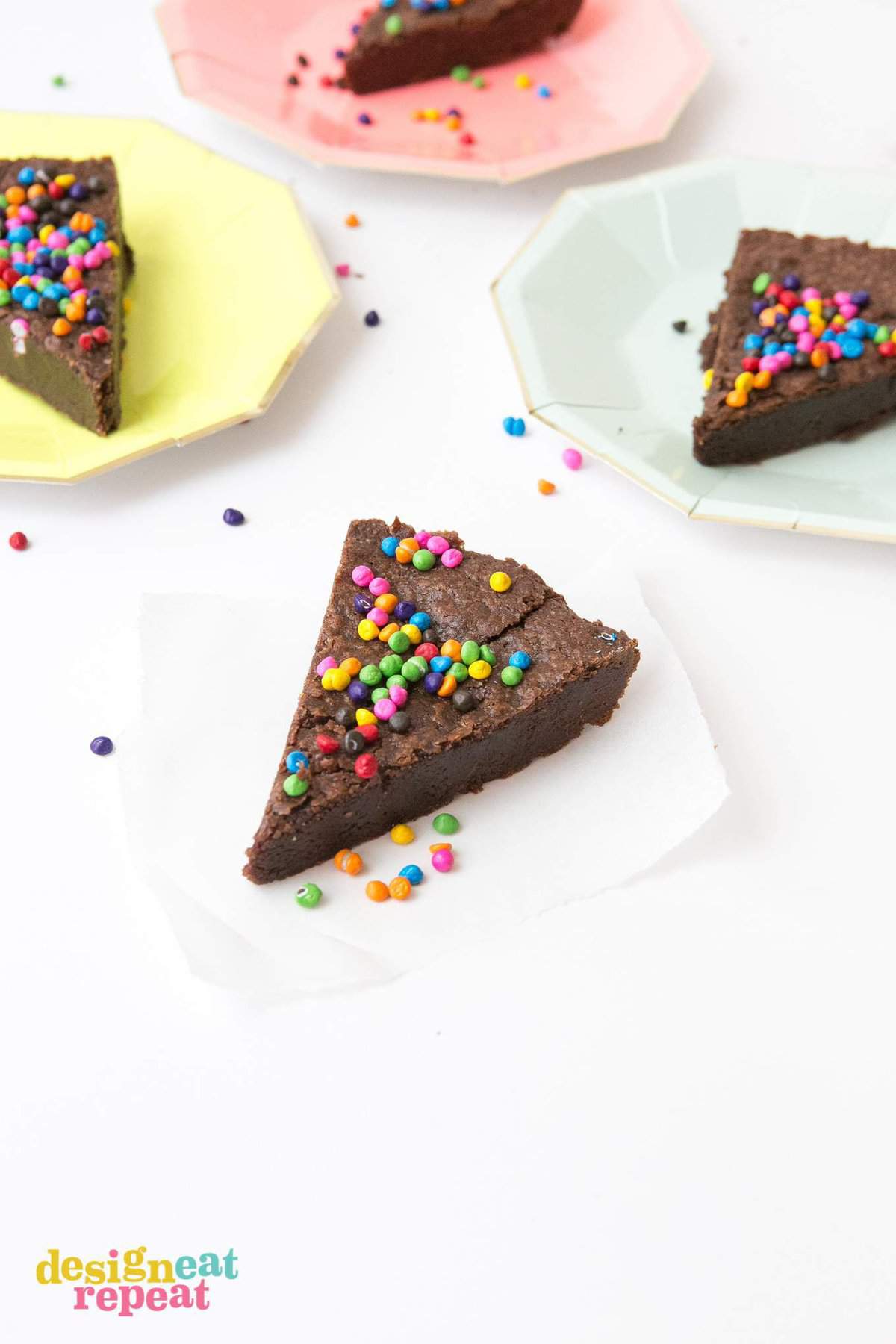 Slice of brownie pie with rainbow chips on piece of parchment paper and rainbow plates.