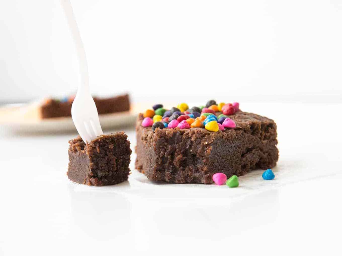 Brownie with rainbow chocolate chips with bite taken out of it with fork.
